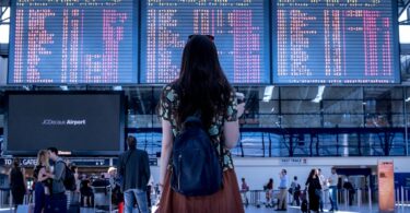 Tableau d'affichage d'un gare devant une voyageuse hésitante