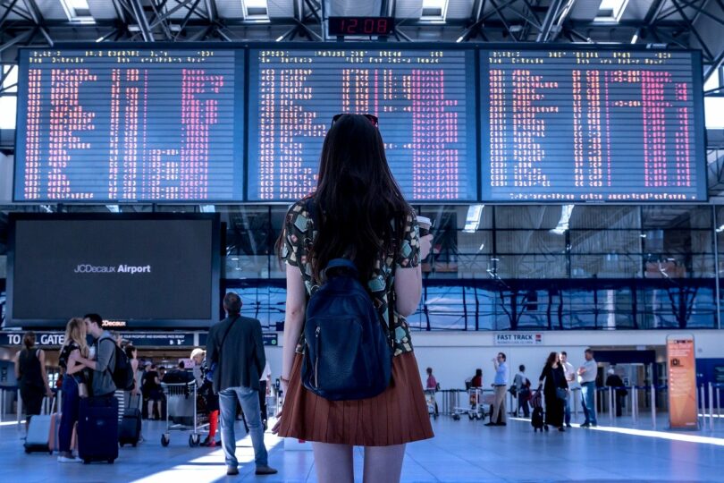 Tableau d'affichage d'un gare devant une voyageuse hésitante